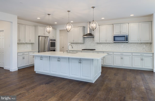 kitchen with wall chimney exhaust hood, pendant lighting, appliances with stainless steel finishes, and dark hardwood / wood-style flooring