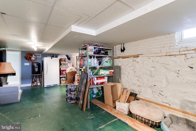 basement with a paneled ceiling and white refrigerator