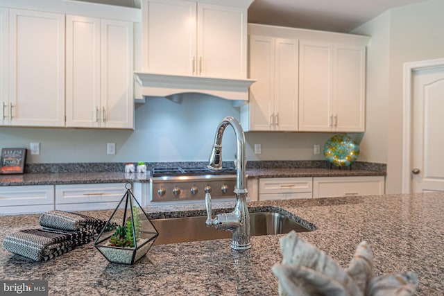 kitchen featuring dark stone countertops, white cabinetry, and sink