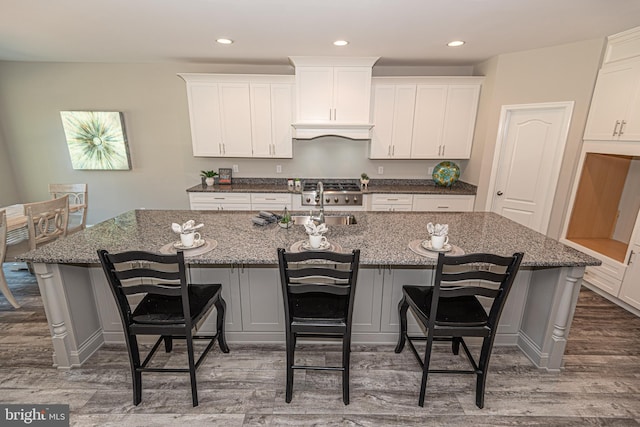 kitchen with dark hardwood / wood-style flooring, a kitchen bar, an island with sink, and white cabinets