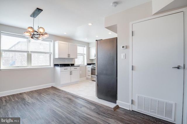 kitchen featuring pendant lighting, white cabinets, stainless steel refrigerator, light tile flooring, and an inviting chandelier