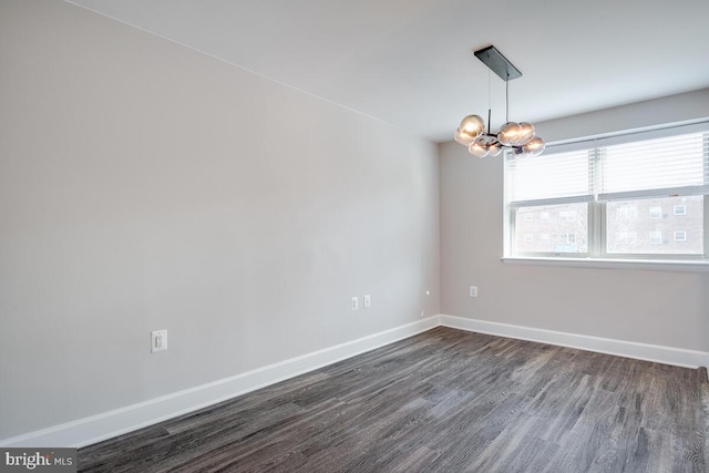 empty room with dark hardwood / wood-style flooring and a notable chandelier