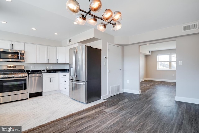 kitchen with white cabinets, decorative light fixtures, wood-type flooring, and stainless steel appliances