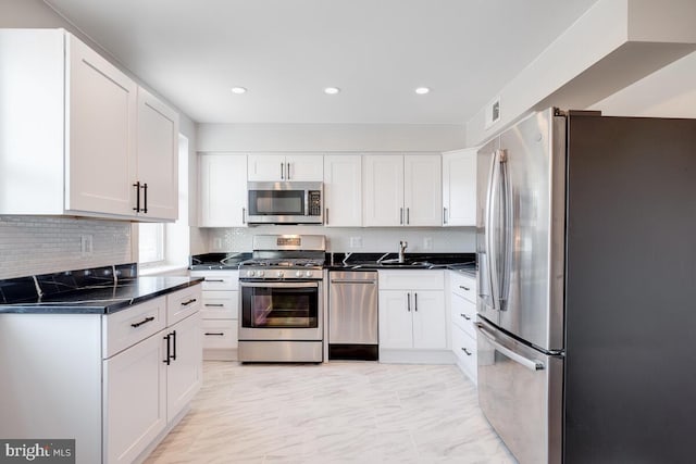 kitchen with light tile flooring, appliances with stainless steel finishes, white cabinetry, backsplash, and sink