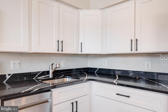 kitchen featuring white cabinetry, stainless steel dishwasher, dark stone countertops, backsplash, and sink