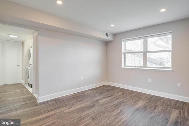 spare room with stacked washing maching and dryer and dark hardwood / wood-style floors