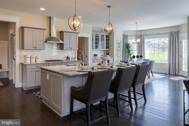 kitchen with gray cabinets, wall chimney exhaust hood, dark wood-type flooring, and decorative light fixtures