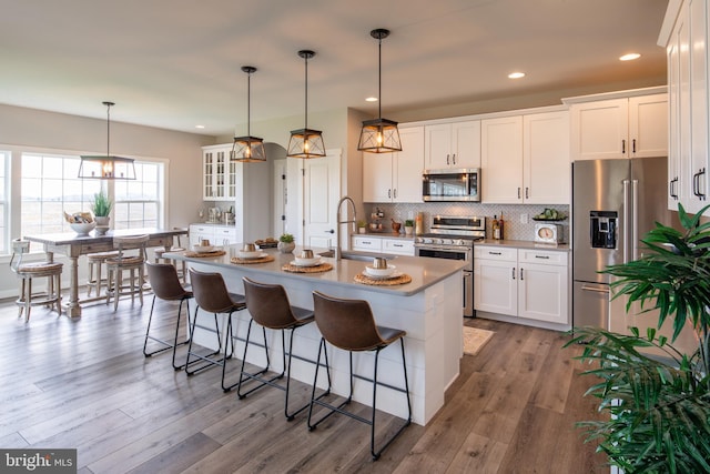 kitchen featuring sink, appliances with stainless steel finishes, a kitchen island with sink, white cabinets, and decorative light fixtures