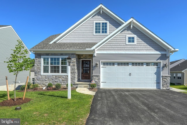 craftsman house featuring an attached garage, driveway, stone siding, roof with shingles, and a front yard