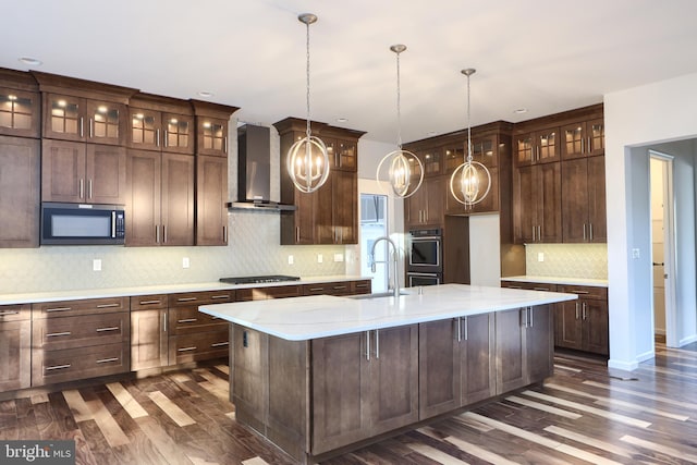 kitchen with tasteful backsplash, wall chimney range hood, a kitchen island with sink, dark hardwood / wood-style floors, and black gas cooktop