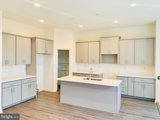 kitchen with a center island with sink, light hardwood / wood-style flooring, sink, and gray cabinets