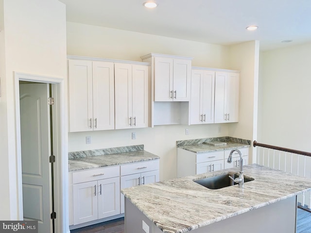 kitchen with dark hardwood / wood-style flooring, white cabinetry, sink, and light stone counters