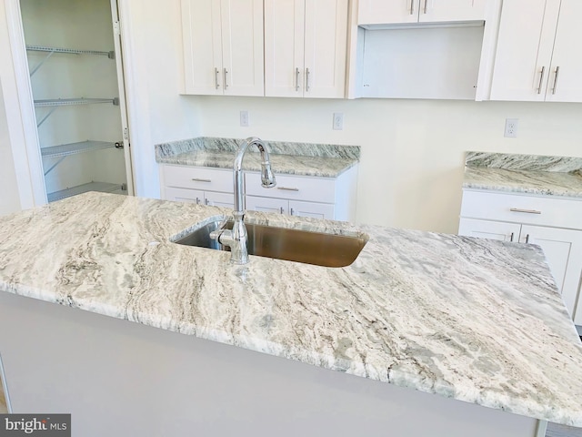 kitchen with light stone countertops, sink, and white cabinetry