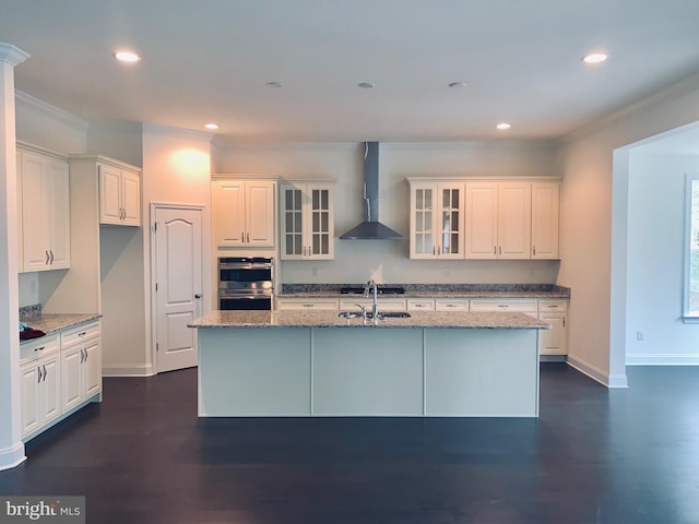 kitchen featuring dark hardwood / wood-style flooring, a kitchen island with sink, double oven, and wall chimney range hood