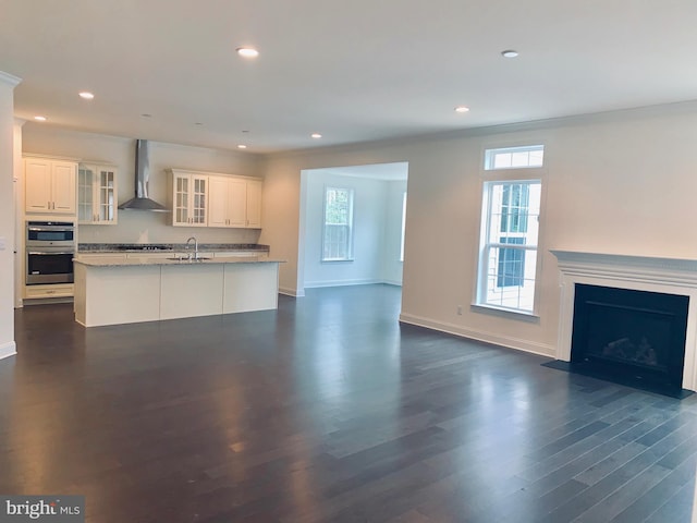 kitchen featuring appliances with stainless steel finishes, wall chimney range hood, light stone counters, dark hardwood / wood-style flooring, and sink