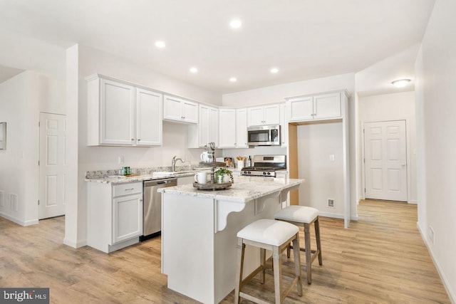 kitchen with a kitchen island, appliances with stainless steel finishes, white cabinets, and light wood-type flooring