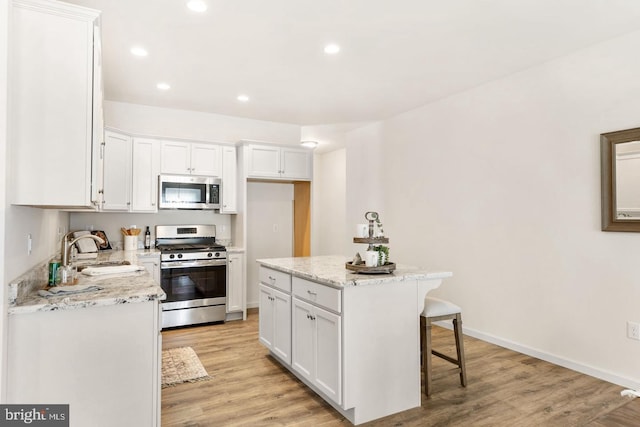 kitchen featuring a center island, stainless steel appliances, white cabinets, and light wood-type flooring