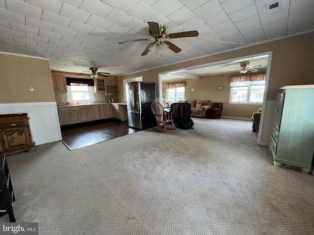 unfurnished living room featuring crown molding, ceiling fan, dark carpet, and sink