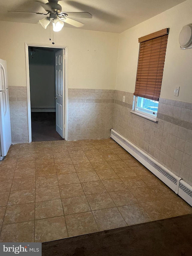 unfurnished room with dark tile flooring, tile walls, a baseboard radiator, and ceiling fan