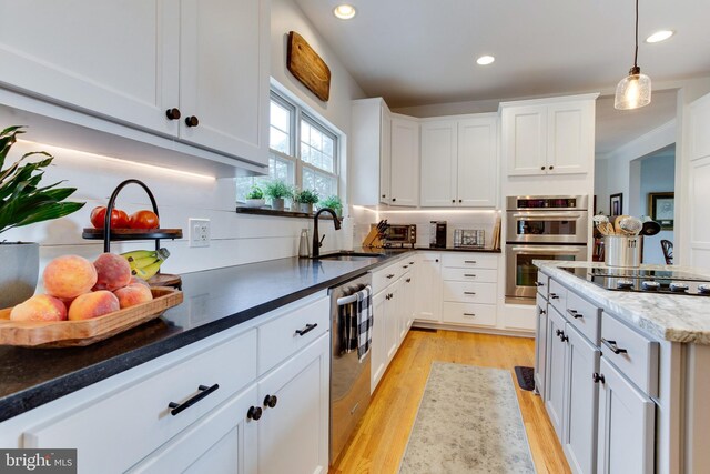 kitchen with dark stone counters, white cabinetry, light wood-type flooring, pendant lighting, and double oven