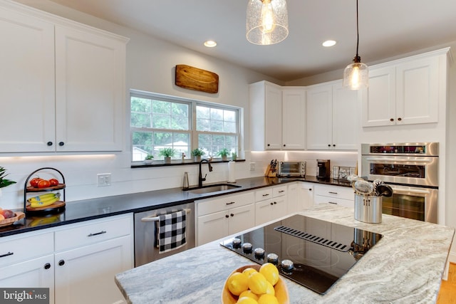 kitchen featuring white cabinetry, hanging light fixtures, sink, stainless steel appliances, and dark stone counters