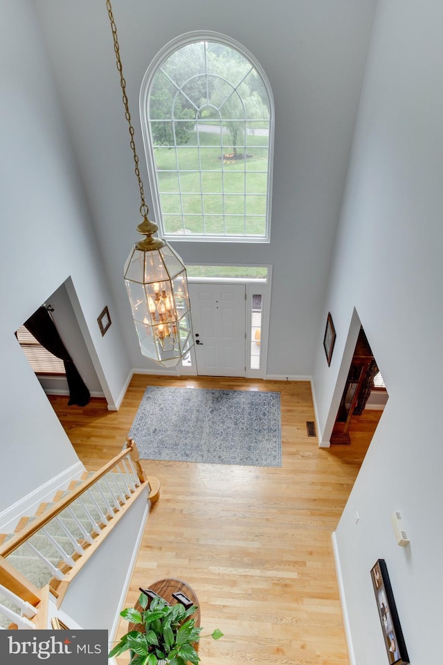 foyer entrance featuring plenty of natural light, an inviting chandelier, a towering ceiling, and light hardwood / wood-style flooring