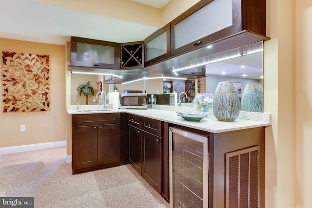 kitchen with sink, wine cooler, light stone counters, dark brown cabinets, and light colored carpet