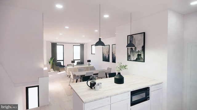 kitchen with light stone countertops, black microwave, light hardwood / wood-style floors, white cabinets, and pendant lighting