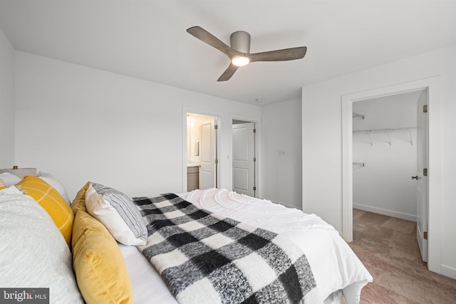 bedroom with a closet, a walk in closet, ceiling fan, ensuite bathroom, and light colored carpet