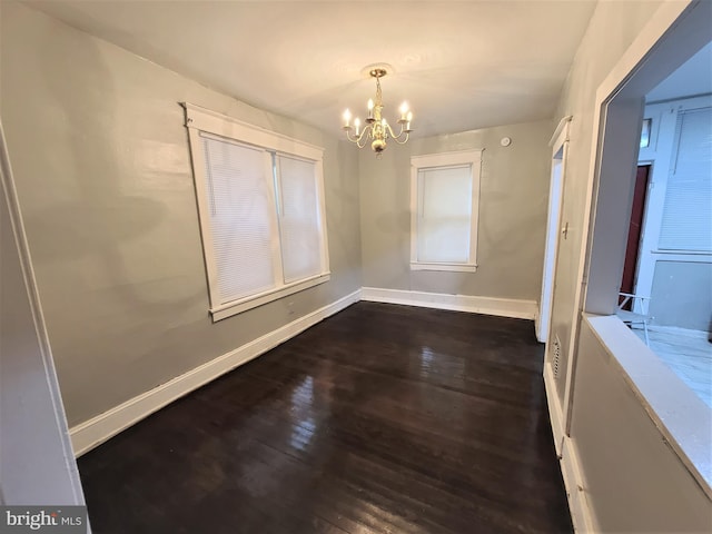 empty room featuring a notable chandelier and dark hardwood / wood-style flooring