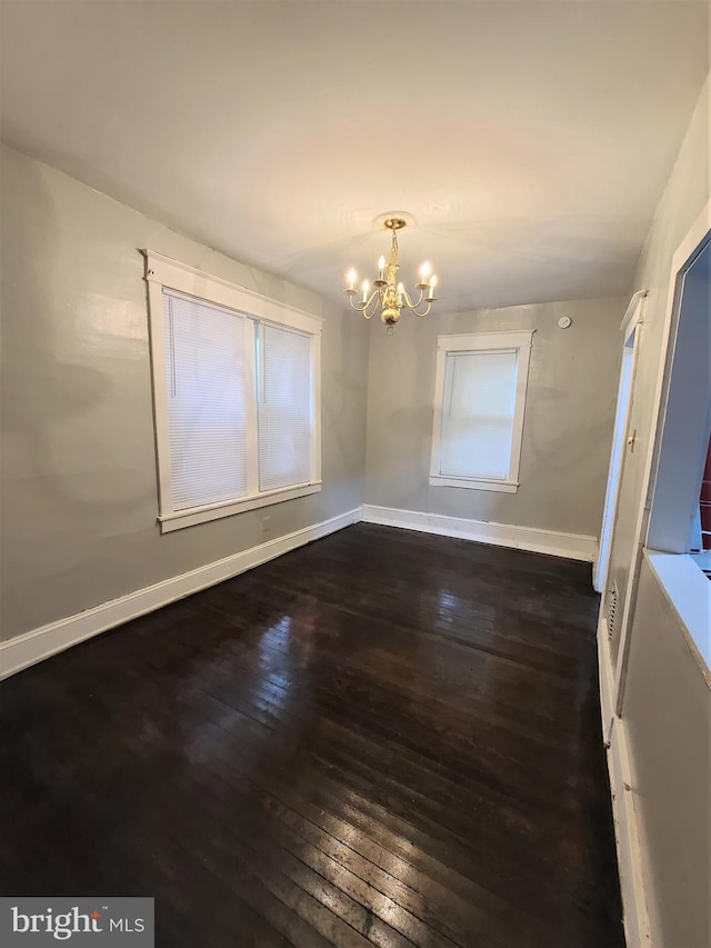 spare room with an inviting chandelier and dark hardwood / wood-style flooring