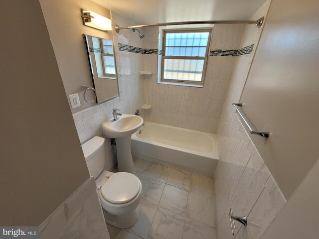 bathroom featuring tile walls, tile floors, toilet, and tiled shower / bath combo