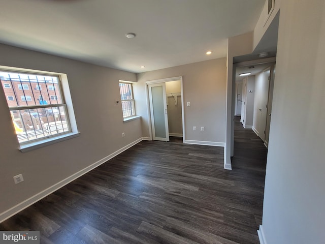 unfurnished bedroom with dark wood-type flooring, a spacious closet, and multiple windows