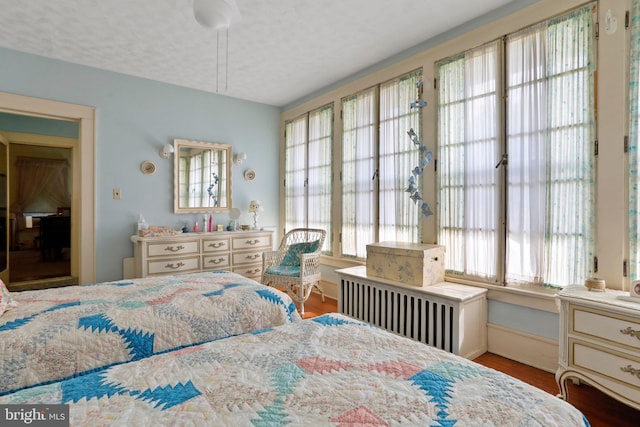 bedroom with hardwood / wood-style flooring, radiator heating unit, multiple windows, and a textured ceiling