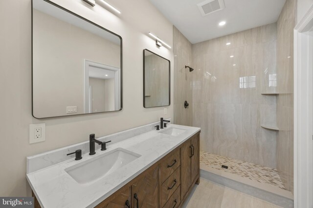 full bath featuring double vanity, visible vents, tiled shower, and a sink