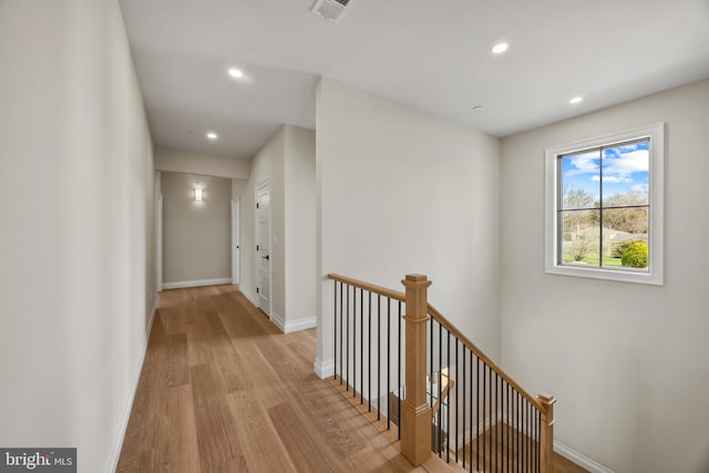 hall featuring baseboards, visible vents, an upstairs landing, and wood finished floors