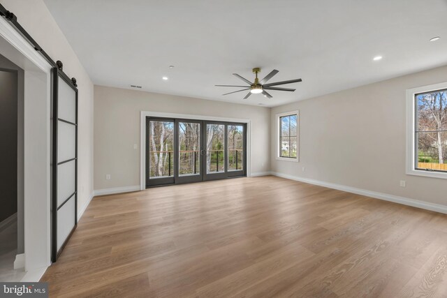 spare room featuring a ceiling fan, a barn door, baseboards, light wood-style floors, and recessed lighting