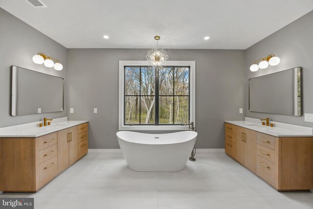 full bath featuring a freestanding bath, a chandelier, a sink, and two vanities