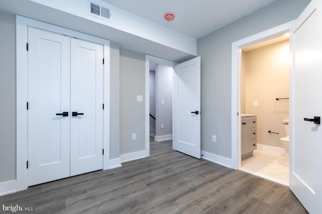 unfurnished bedroom featuring ensuite bathroom, a closet, and hardwood / wood-style flooring