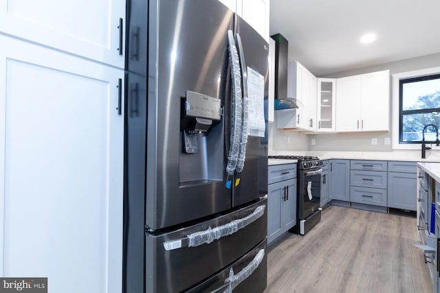 kitchen with gray cabinets, white cabinets, stainless steel appliances, wall chimney range hood, and light wood-type flooring