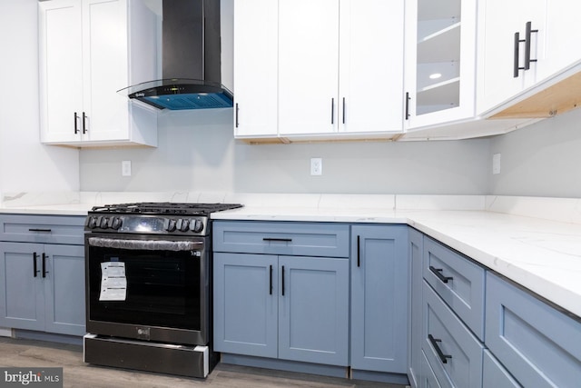 kitchen featuring stainless steel gas stove, light stone counters, light hardwood / wood-style floors, wall chimney exhaust hood, and white cabinets