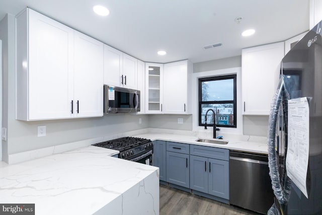 kitchen featuring light stone countertops, hardwood / wood-style floors, black appliances, white cabinets, and sink