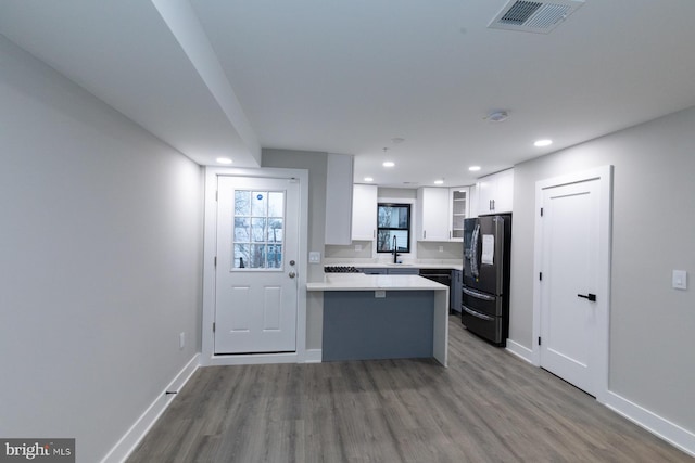 kitchen with black fridge, hardwood / wood-style flooring, white cabinets, kitchen peninsula, and sink