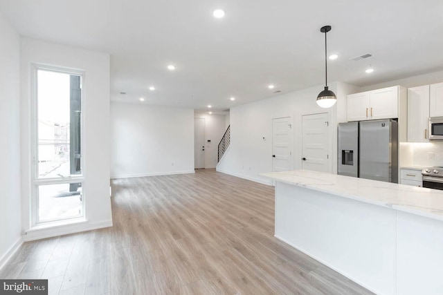 kitchen with light hardwood / wood-style floors, stainless steel appliances, white cabinets, hanging light fixtures, and light stone counters