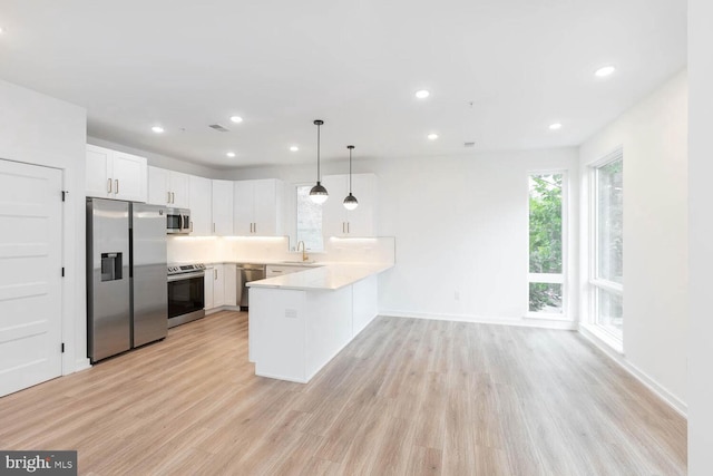 kitchen with kitchen peninsula, stainless steel appliances, pendant lighting, and light wood-type flooring