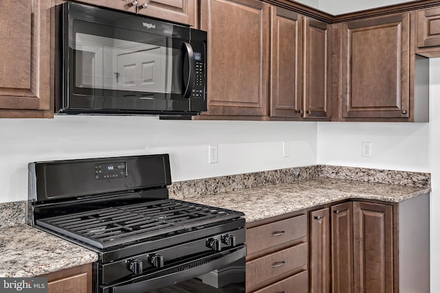 kitchen featuring dark brown cabinets, light stone counters, and black appliances