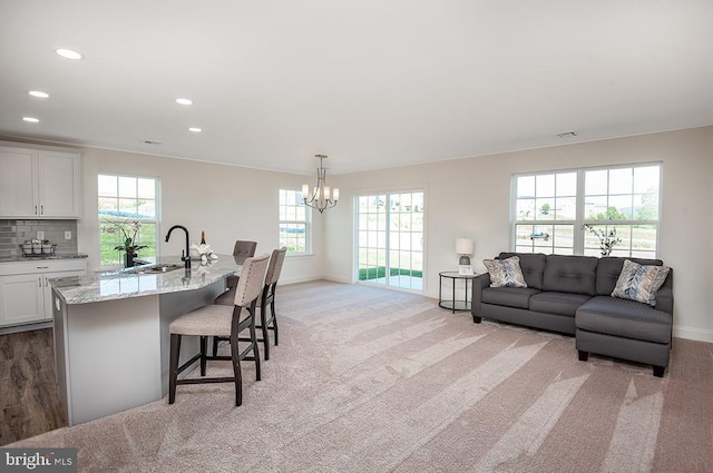 kitchen with an inviting chandelier, tasteful backsplash, light colored carpet, light stone countertops, and white cabinets