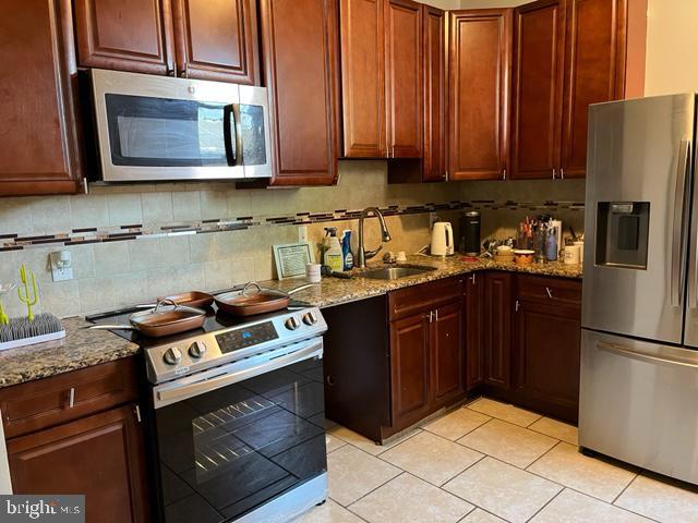 kitchen with backsplash, light stone countertops, appliances with stainless steel finishes, and sink