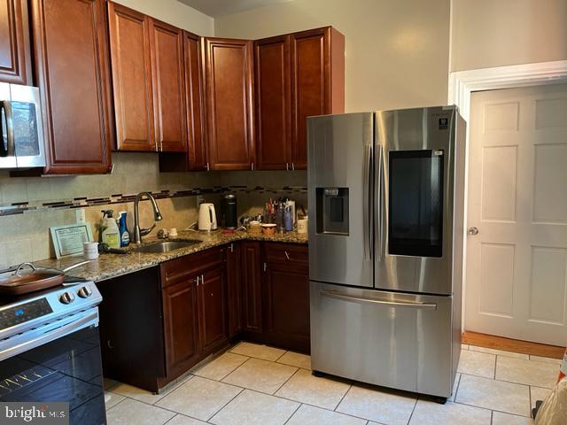 kitchen with light stone counters, tasteful backsplash, light tile floors, stainless steel appliances, and sink