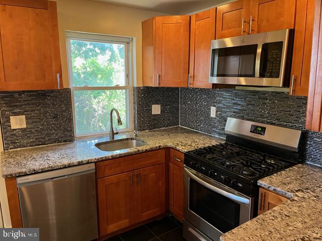 kitchen with backsplash, appliances with stainless steel finishes, light stone countertops, and sink